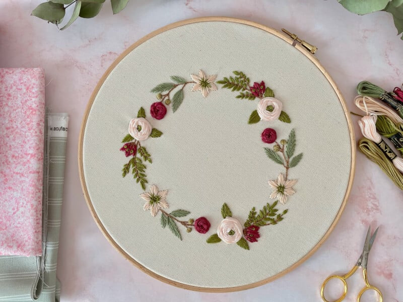 A ring of roses on white fabric held in an embroidery hoop.